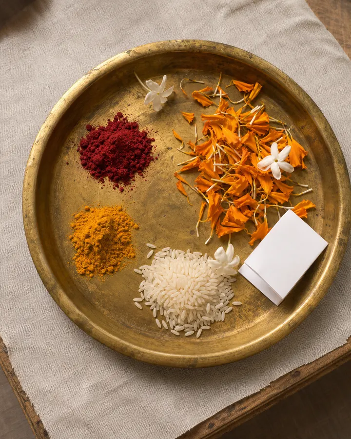 The offering thali seen from above — flowers, a lamp, akshat and a folded leaf.