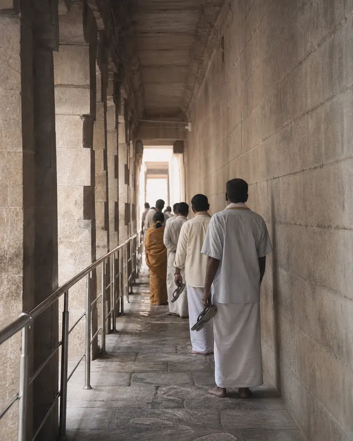 A quiet temple corridor of worn stone with the queue rail running along it in early light.