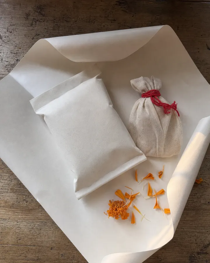 A sealed prasadam packet and a printed slip resting in an open postal box on brown paper.